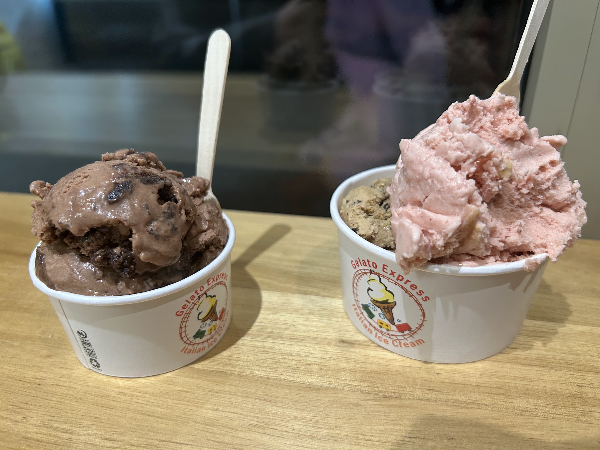 Two cups of gelato with chocolate and strawberry flavors in branded cups