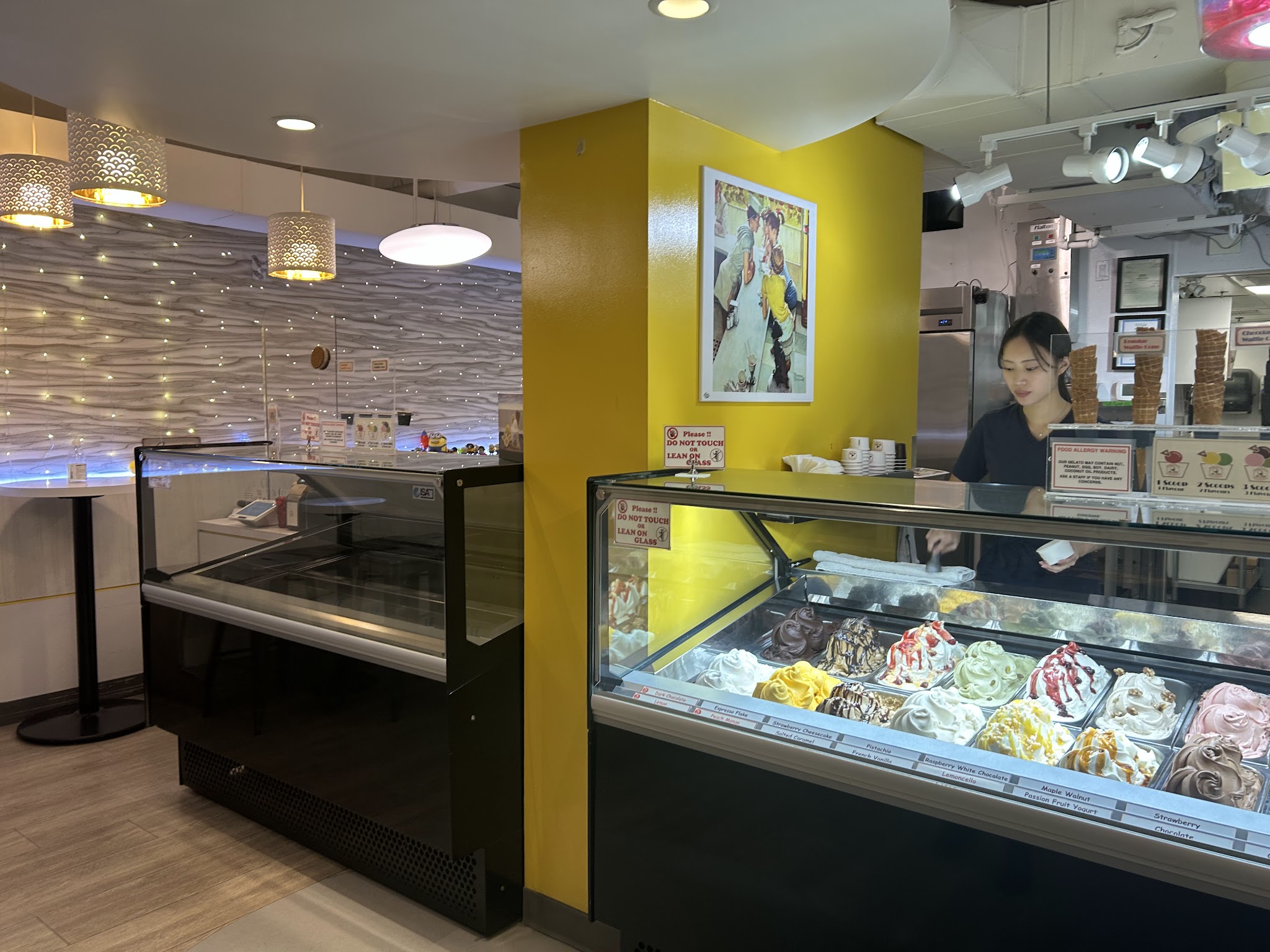Interior of Gelato Express showing the counter area, gelato display case, yellow accent wall, and warm pendant lighting