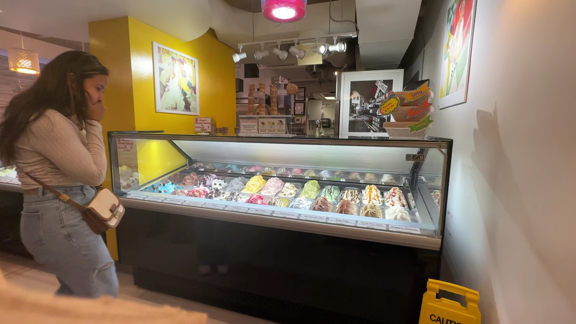 Customer browsing the gelato display case with colorful flavors and art on walls