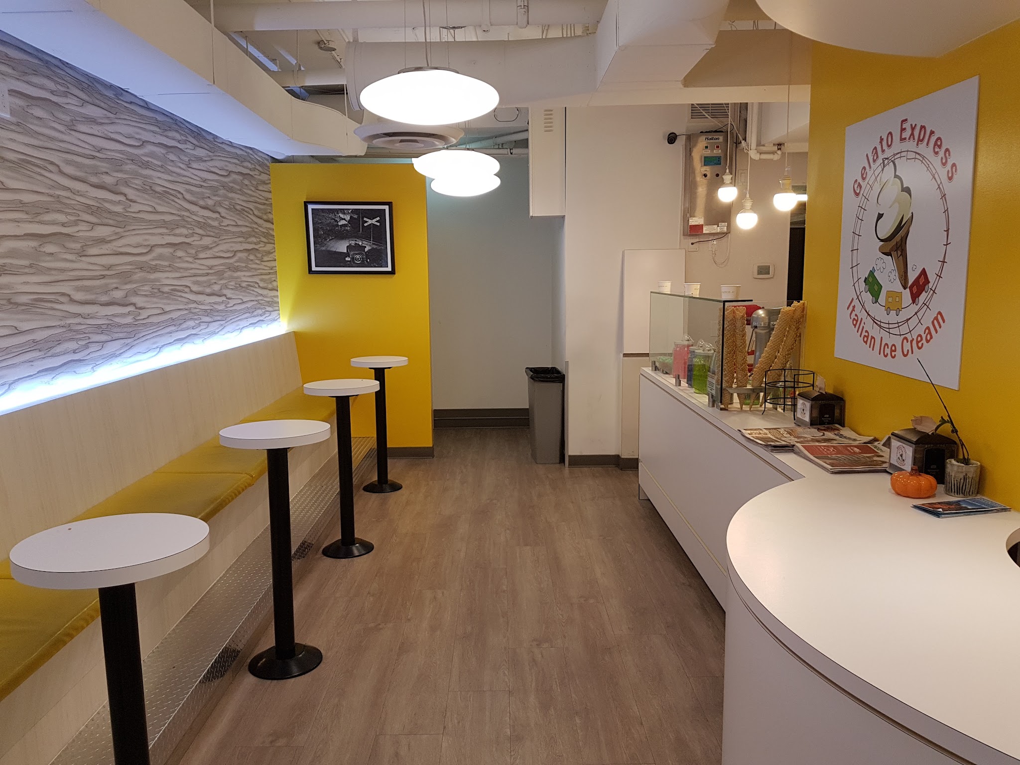 Wide interior view with yellow walls, seating area, and gelato preparation counter